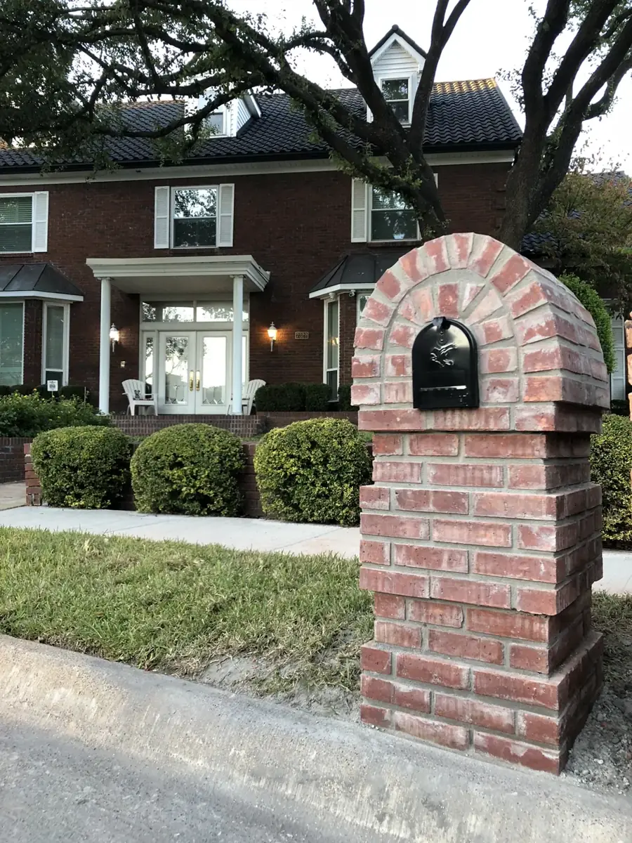 Arched red brick mailbox in front of a brick colonial home