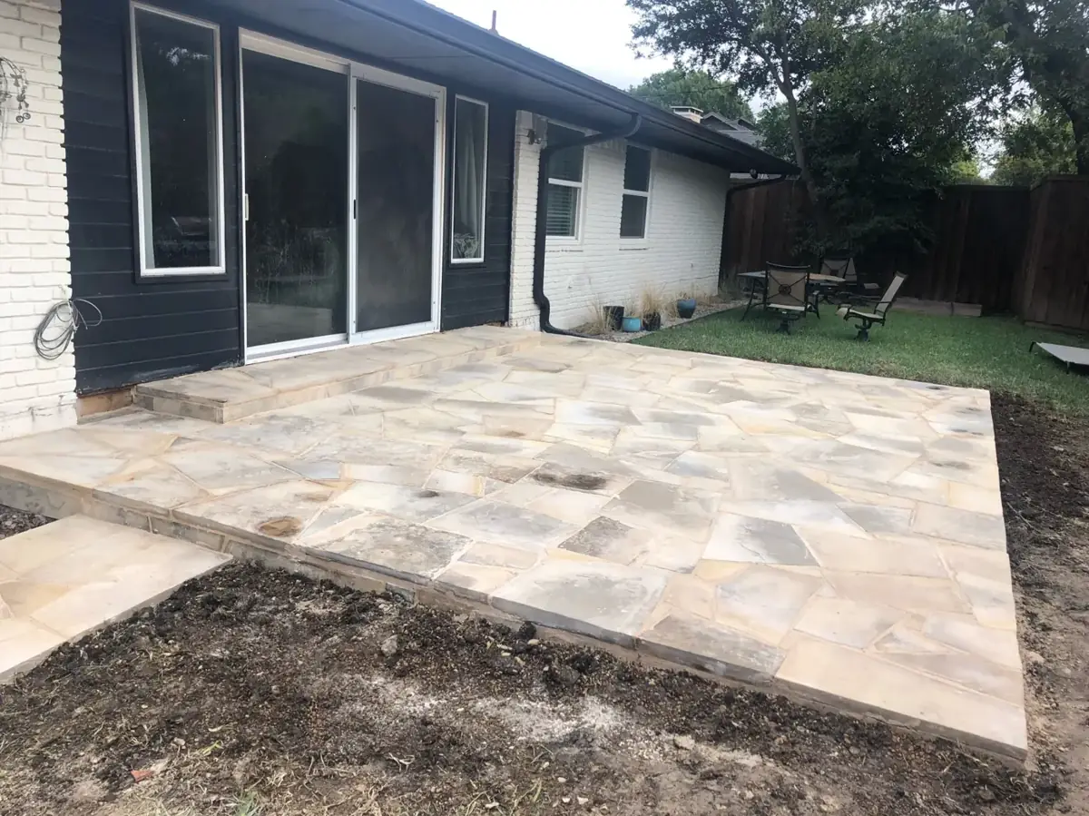 New flagstone patio outside the back doors of a white and navy home