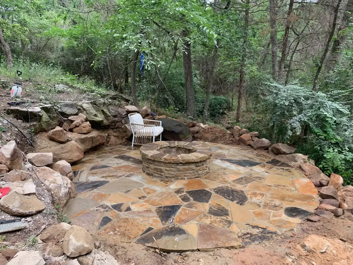 Flagstone patio with a round stone fire pit in a wooded backyard, built by Omega Masonry