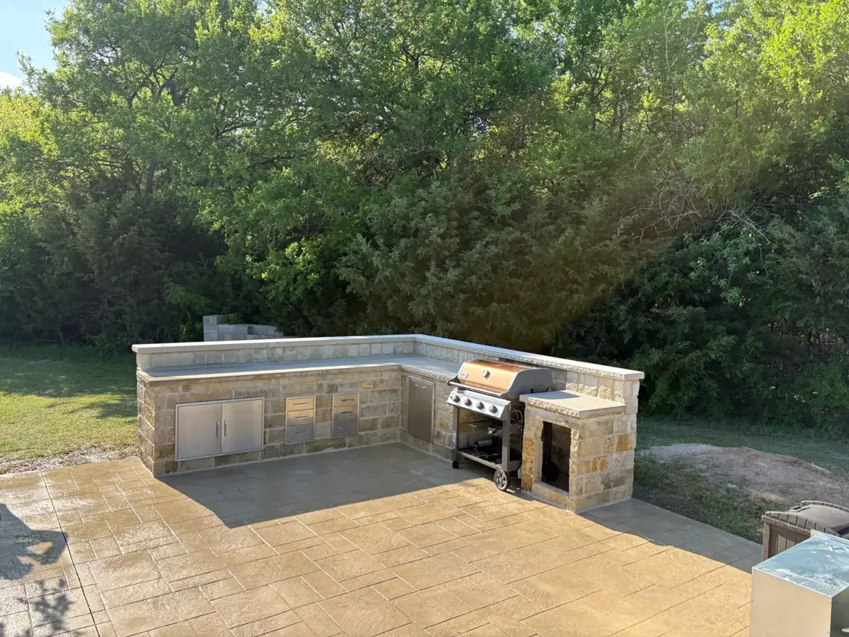 L-shaped stone outdoor kitchen with a built-in grill on a stamped concrete patio