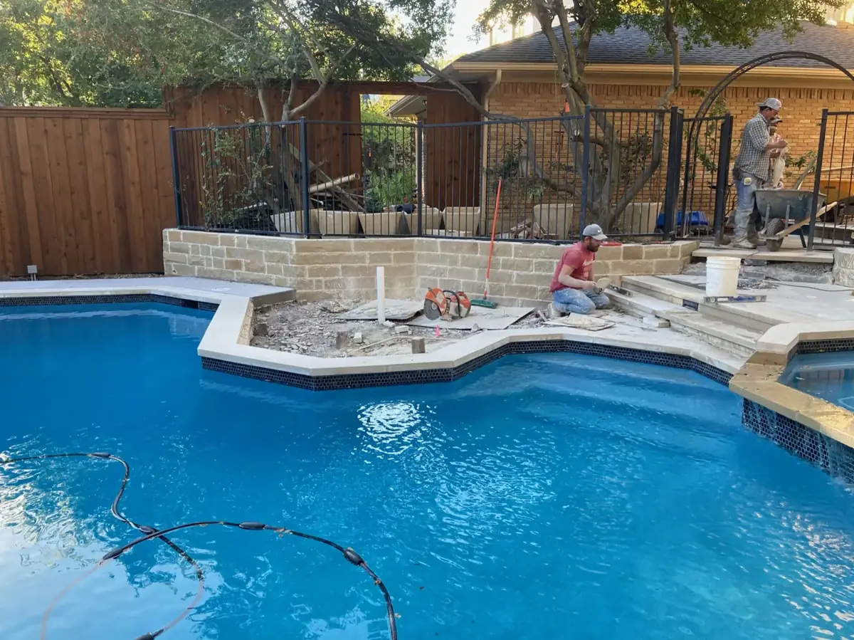 Omega Masonry crew installing stone coping and a raised wall on a new pool